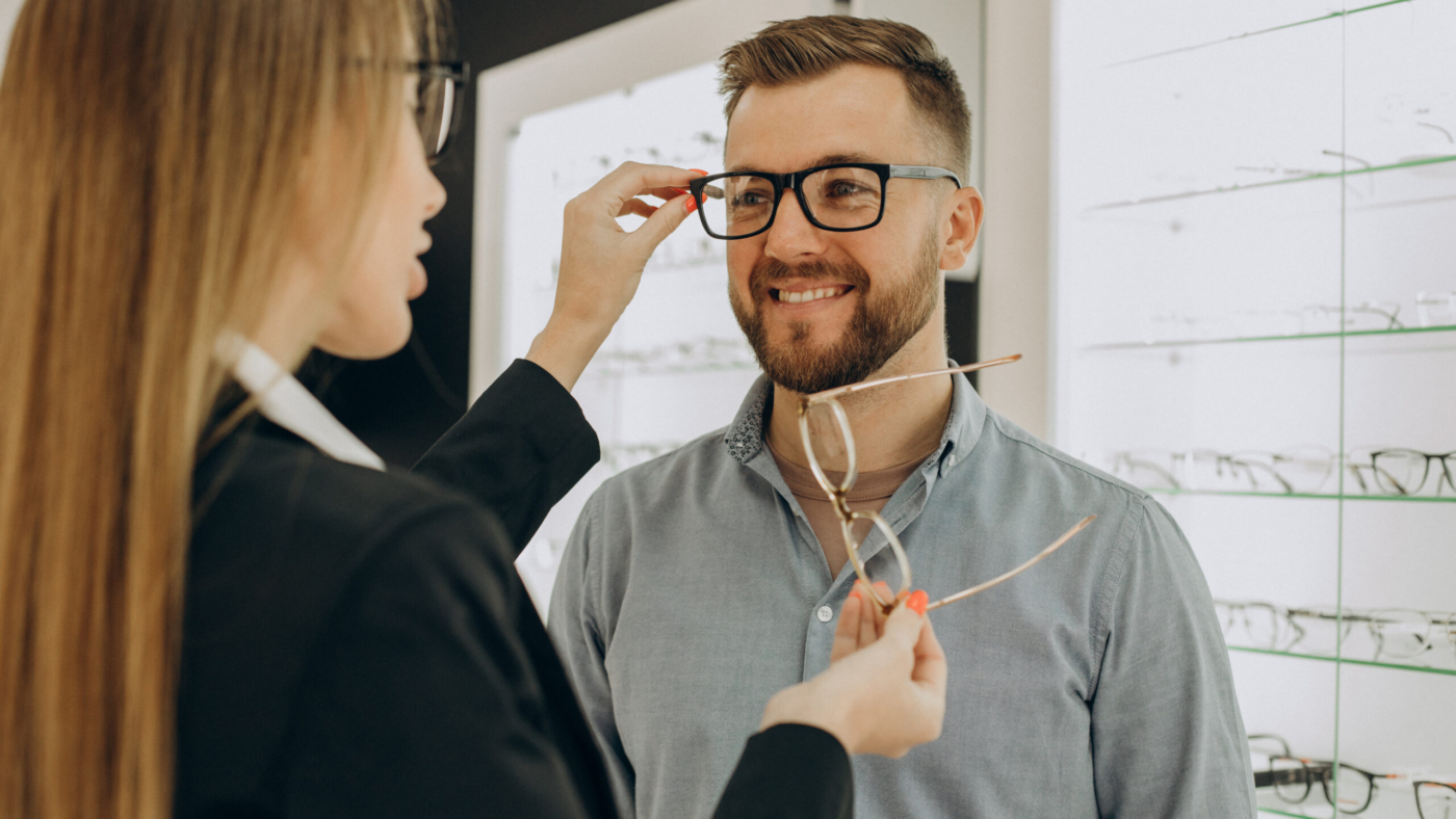 Customer shoosing spectacles at optic store with the lelp of sales person