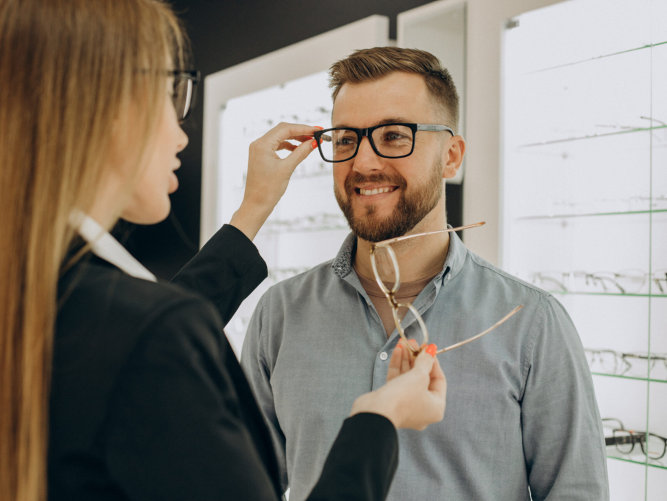 Customer shoosing spectacles at optic store with the lelp of sales person